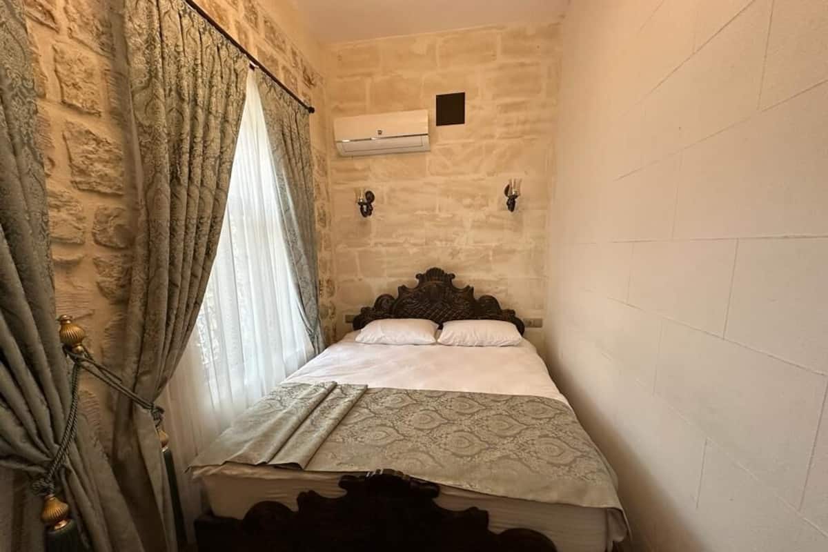 Une petite pièce avec un lit, des murs en pierre et une fenêtre avec des rideaux.