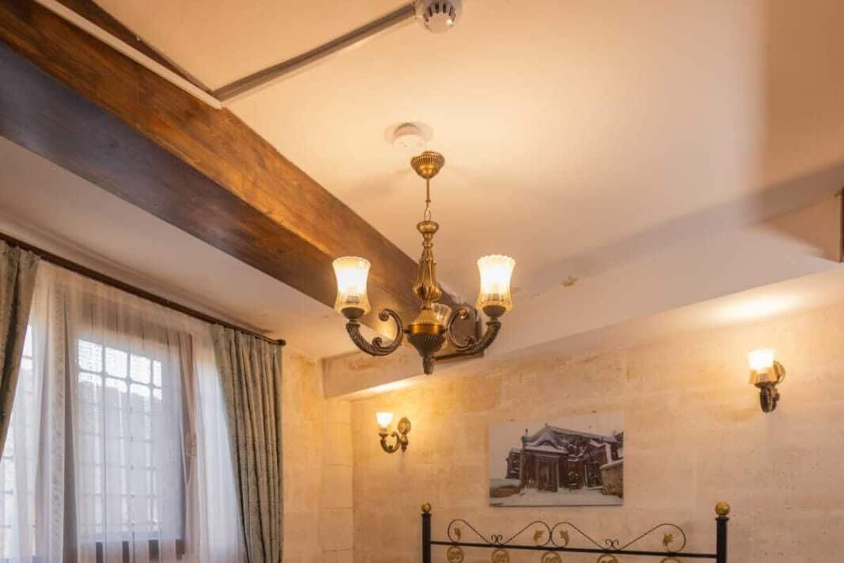 Une chambre à coucher avec un lit, un lustre, une applique murale, une fenêtre avec des rideaux et un tableau au mur.