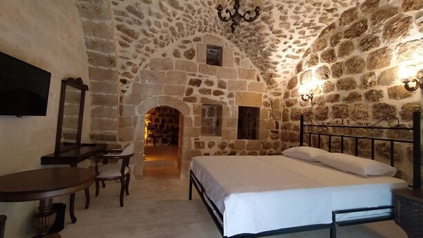 A stone-walled room with a bed, a desk, and a chair. - ARUR KONAGI (Mardin)