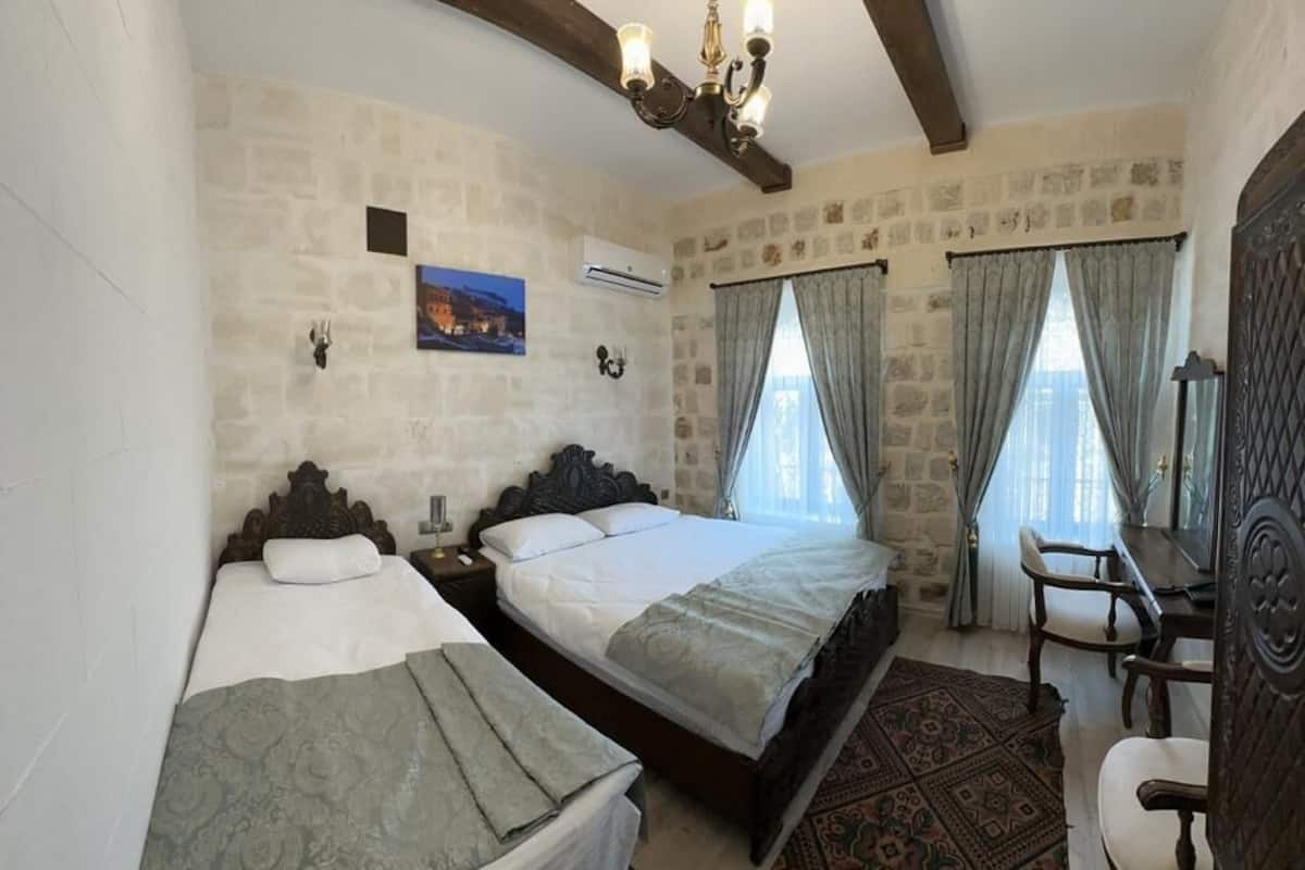 Une chambre à coucher avec un grand lit, deux petits lits, une chaise en bois, un bureau et un lustre.