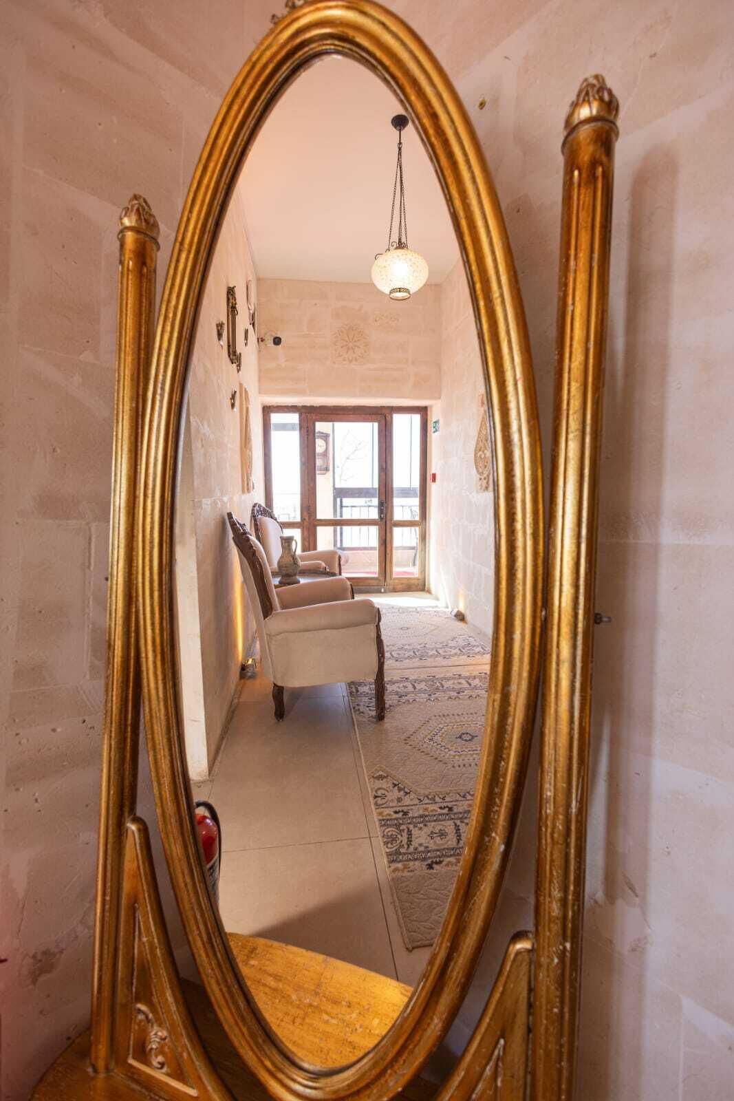 Una habitación con un espejo grande y ornamentado, una silla de madera, un tapete estampado y una puerta que da a otro espacio.