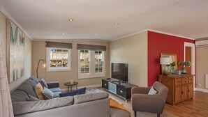 Een woonkamer met een grijze bank, een klein rond tafeltje, een televisie en een kast met decoratieve objecten.