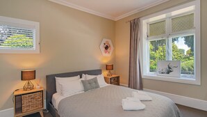 Een slaapkamer met een bed, twee nachtkastjes met lampen, een raam met gordijnen en kunst aan de muren.