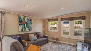 Een woonkamer met een grijze bank, een klein rond tafeltje en een groot raam met uitzicht op groen.