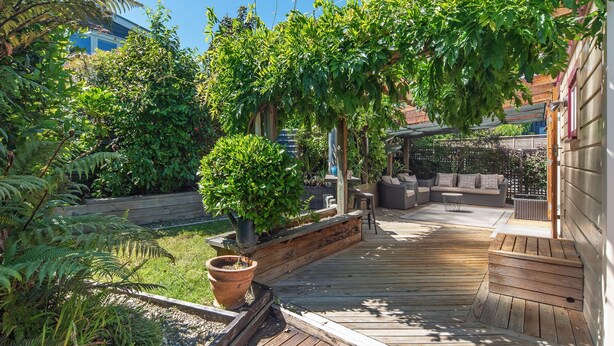 Een houten terras met een ingebouwde zithoek en een pergola begroeid met klimplanten.
