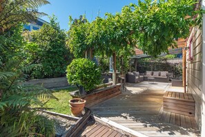 A wooden deck with a built-in seating area and a pergola covered with climbing plants. - Birdsong Cottage (Nelson)