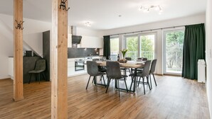 Eine moderne Küche mit weißen Schränken, ein Essbereich mit Holztisch und -stühlen sowie eine große Schiebeglasdoor zum Balkon.