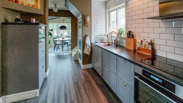 Een moderne keuken met grijze kastjes, een roestvrijstalen afzuigkap en een raam voor natuurlijk licht.