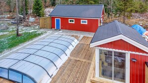 Een kas met een transparant dak, een rood gebouw met een blauwe deur en een houten terras.