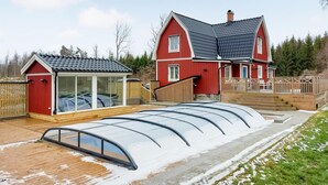 Een rode woning met een grote glazen kas en een houten terras.