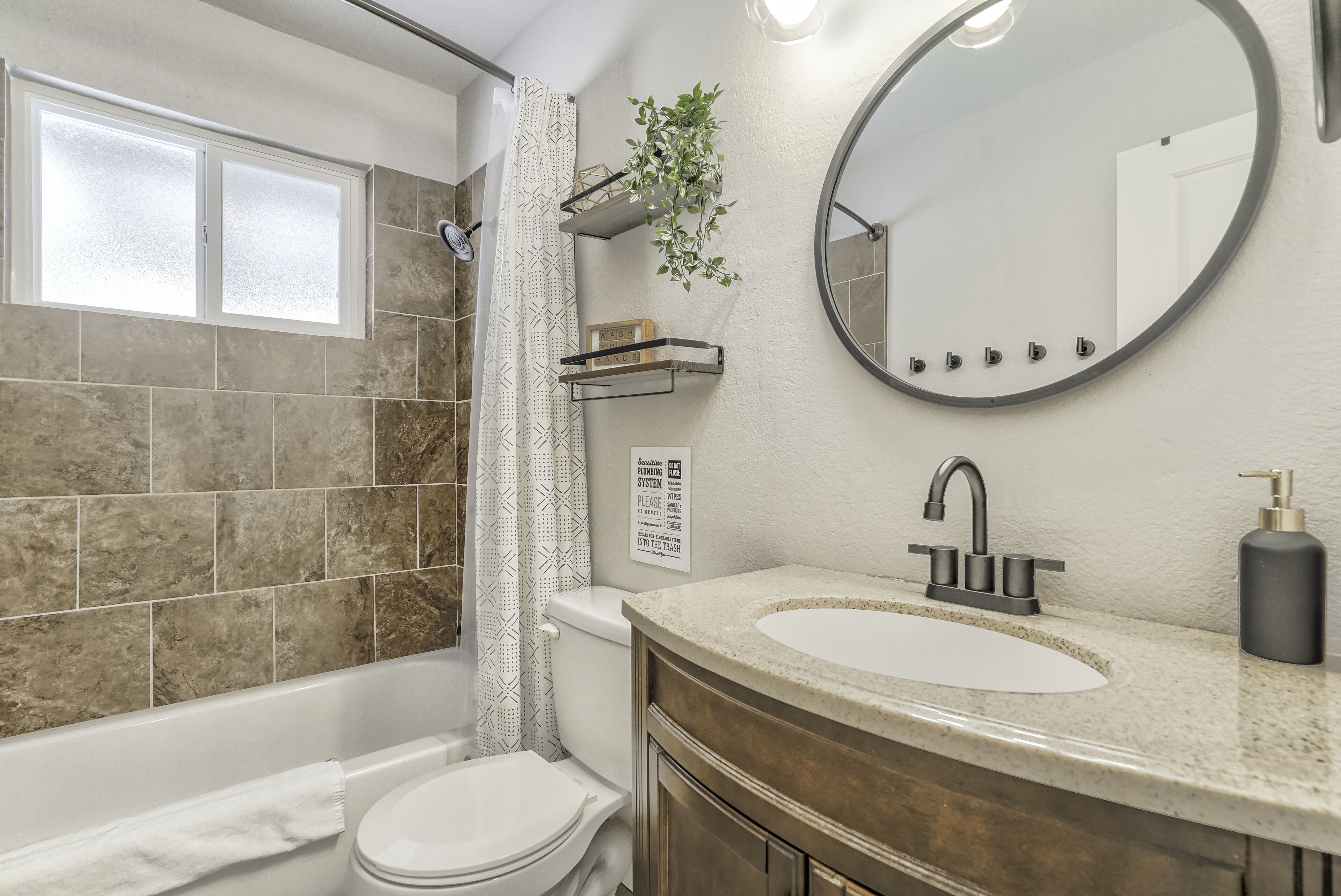 Un baño moderno con bañera, inodoro y lavamanos. Hay una cortina de ducha, un espejo y una planta en un estante.