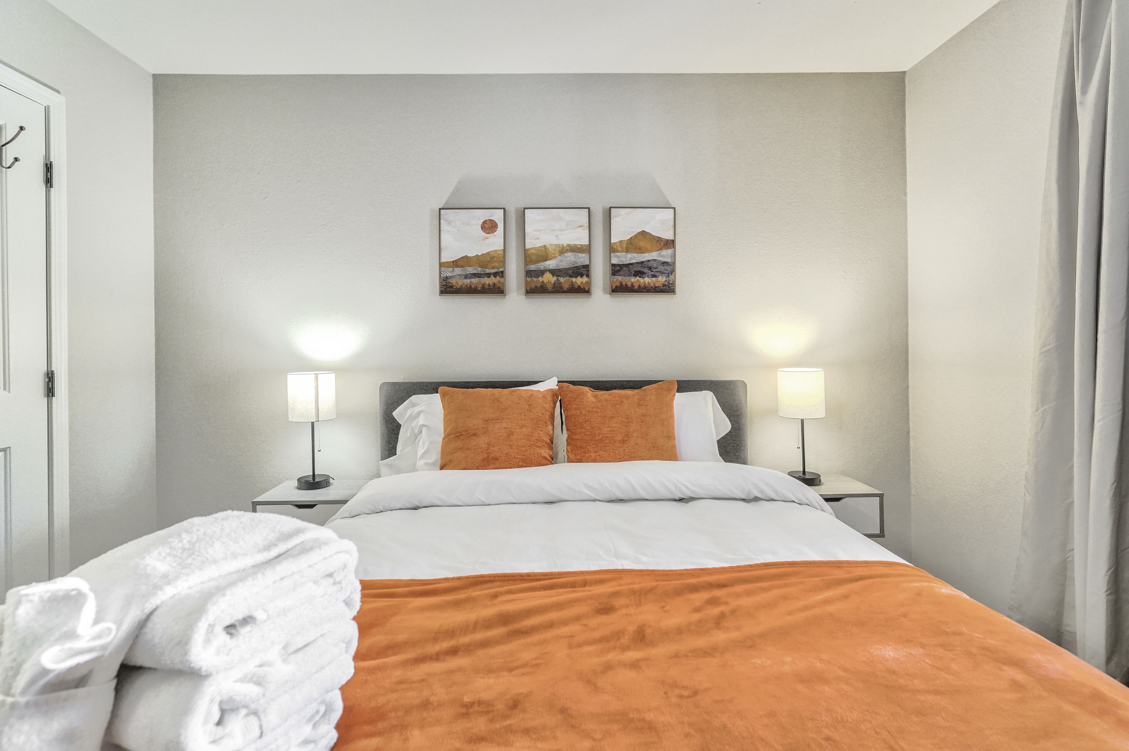 A hotel room with a bed, two bedside lamps, a nightstand, and a wall-mounted artwork.