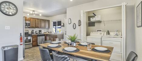 Una cocina moderna con armarios de madera, horno empotrado y comedor con mesa de madera y sillas negras.