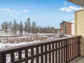 A balcony with a view of a snowy landscape, a brick building, and a yellow car. - Rukachalet 2407 by Interhome (Kuusamo)