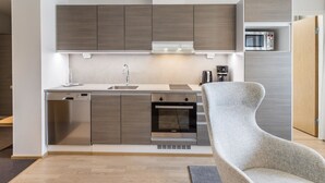 A modern kitchen with built-in appliances, a grey upholstered chair, and a wooden floor.