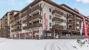 A multi-story hotel with balconies, ski rental shops, and a ski lift visible in the background.