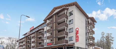 A multi-story hotel with balconies, a ski lift in the background, and a snowy landscape.