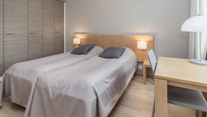 A bedroom with two beds, a wooden wardrobe, a desk, and two bedside lamps.