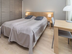 A double bed with a wooden headboard and two bedside lamps, a wooden desk, and a wardrobe with a mirrored door. - Rukachalet 2407 by Interhome (Kuusamo)