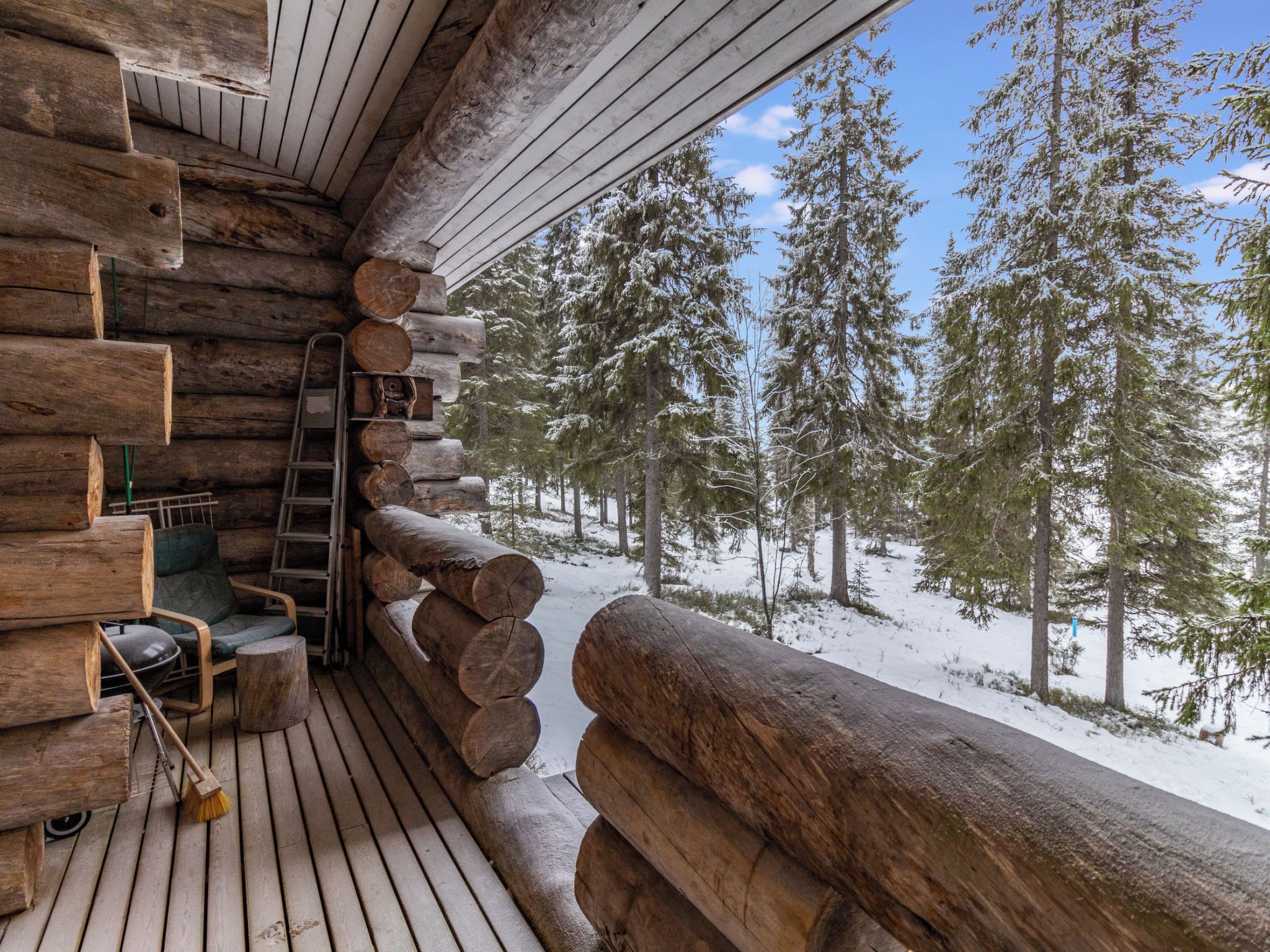 A log cabin with a wooden deck, a ladder, and a chair.