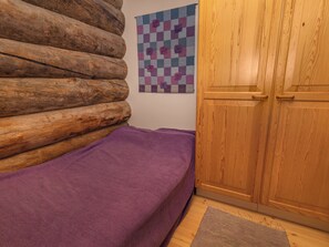 Ein Zimmer mit einer Holzwand, einer violetten Bettdecke, einem karierten Wandbehang und einem Holzschrank.