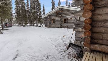 Eine Blockhütte mit einem schnee bedeckten Hof, einer Leiter und einem geparkten Fahrzeug.