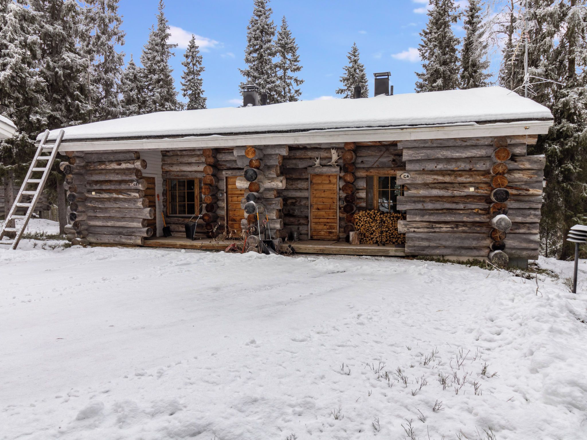 Une cabane en rondins avec un toit enneigé, une véranda en bois et une cheminée bien visible.