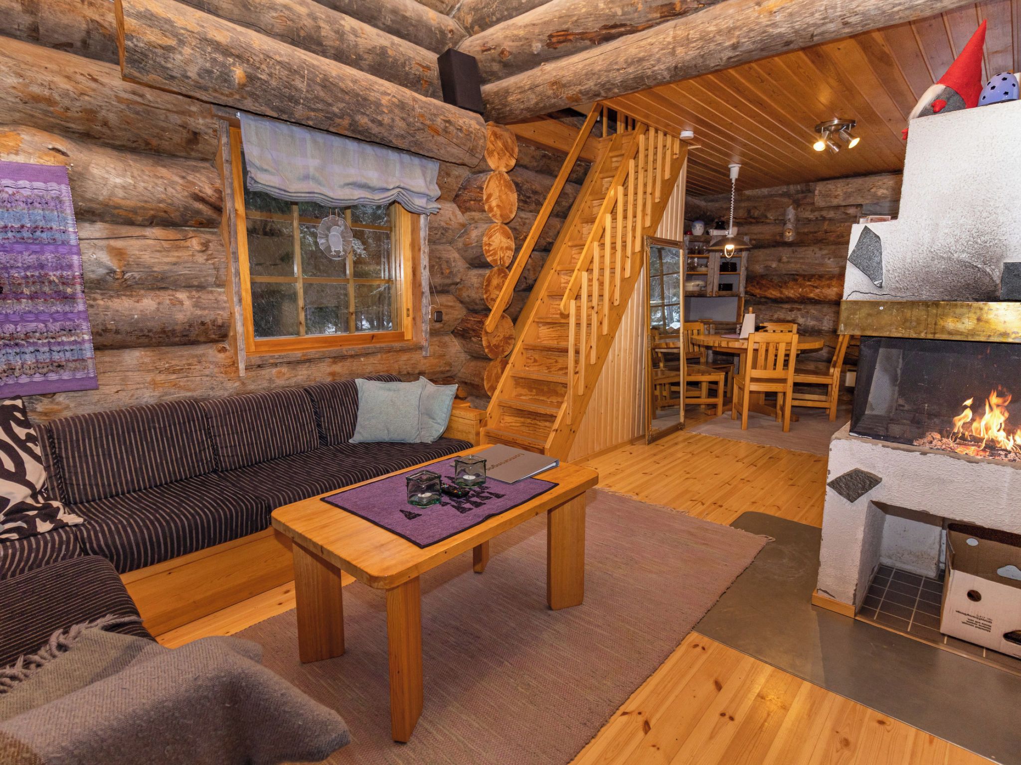 Ein gemütliches Blockhaus-Interieur mit einer Couch, einem Holztisch, einem Kamin und einer Treppe zu einer oberen Ebene.