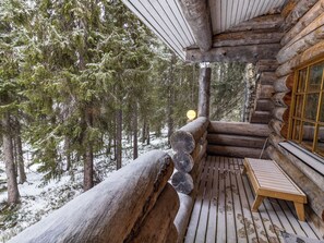 A log cabin with a wooden deck, a bench, and a view of snow-covered trees. - Aurinko-ruka c6 by Interhome (Kuusamo)