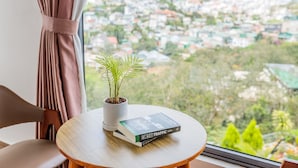 A round wooden table with a potted plant and a book titled "MAT TRAFFIC" in front of a window overlooking a residential area.