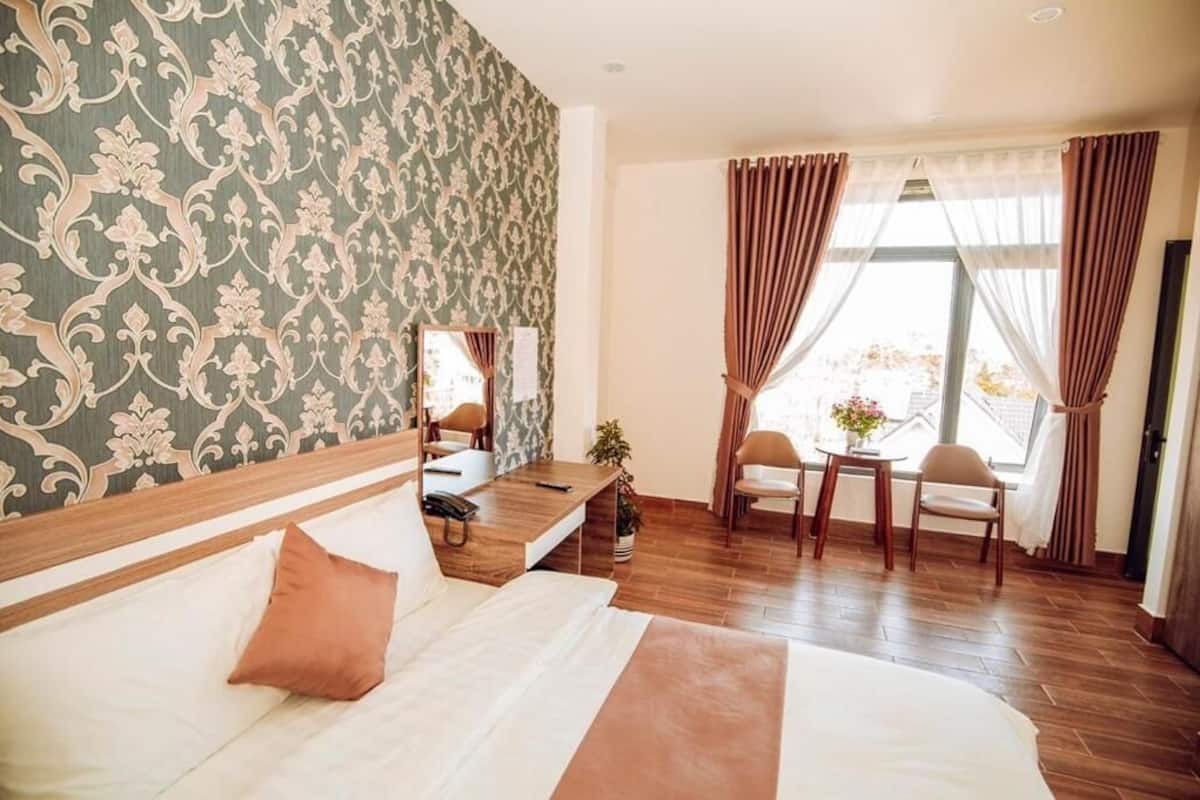 A hotel room with a bed, bedside table, chair, and a small table with a plant.