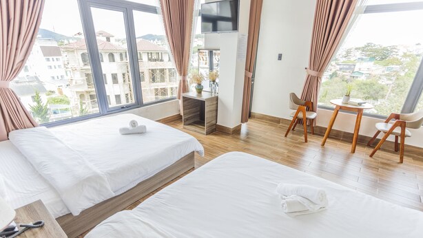 A hotel room with two beds, a desk with a chair, a TV, and a view of the city.