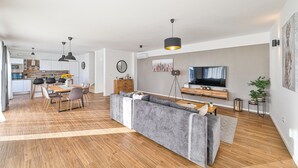 Un espace de vie moderne à aire ouverte comprenant une cuisine, un coin repas et un salon avec un canapé gris et un téléviseur.