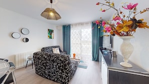 Un salon moderne comprenant un canapé, un coin repas, une grande fenêtre avec des rideaux et un vase décoratif avec des fleurs.