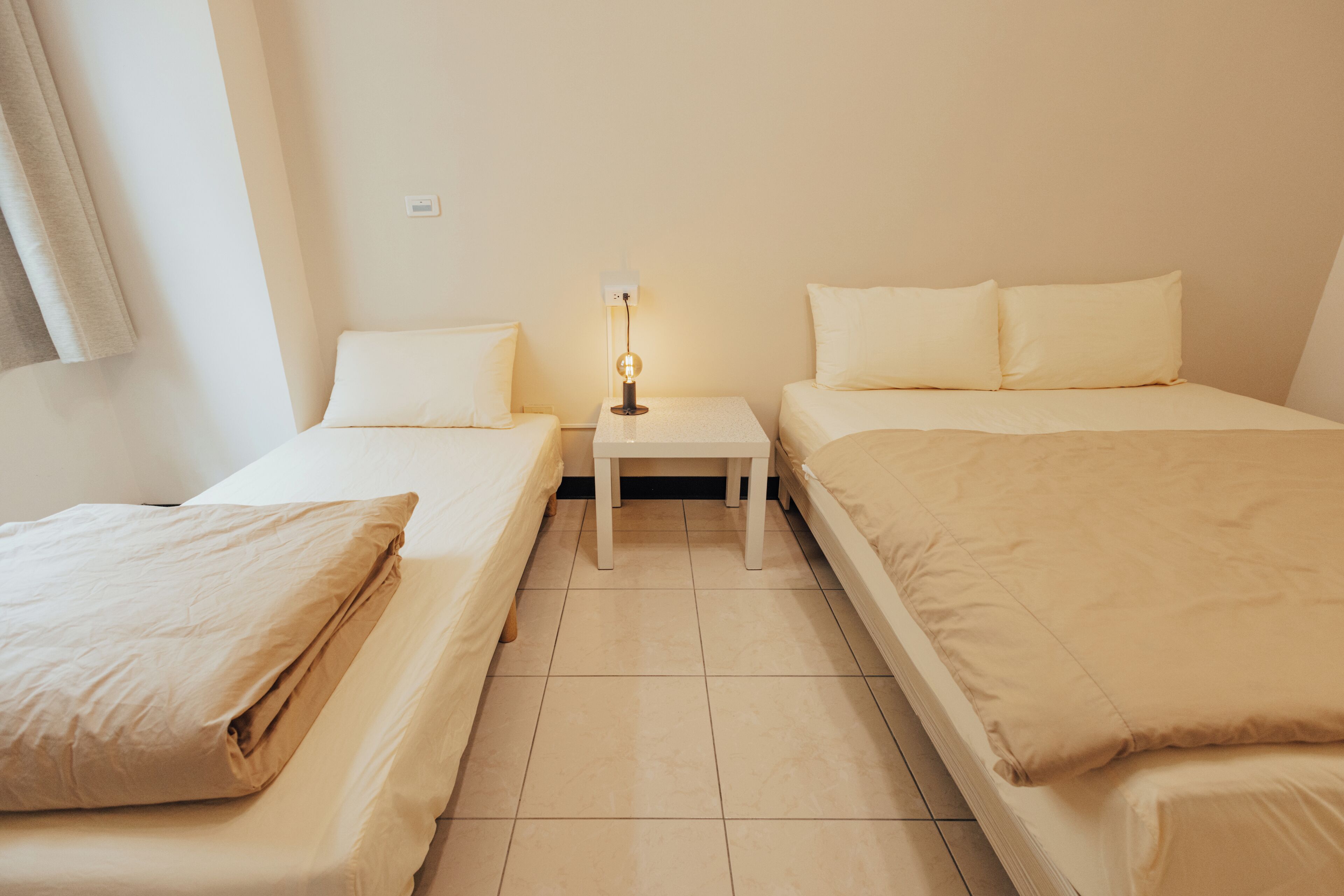 A room with two single beds, a nightstand with a lamp, and a wall socket.