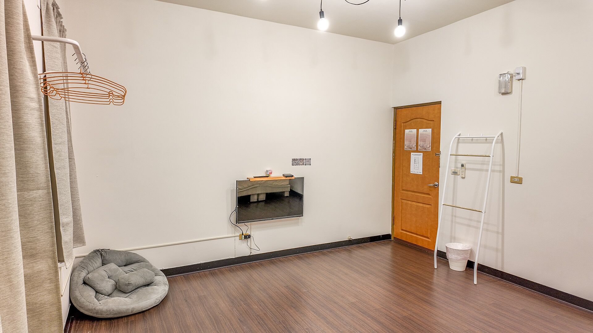 Une pièce avec un plancher en bois, un fauteuil en forme de sac de haricots de couleur grise, un téléviseur blanc fixé au mur, une porte en bois et une échelle blanche.