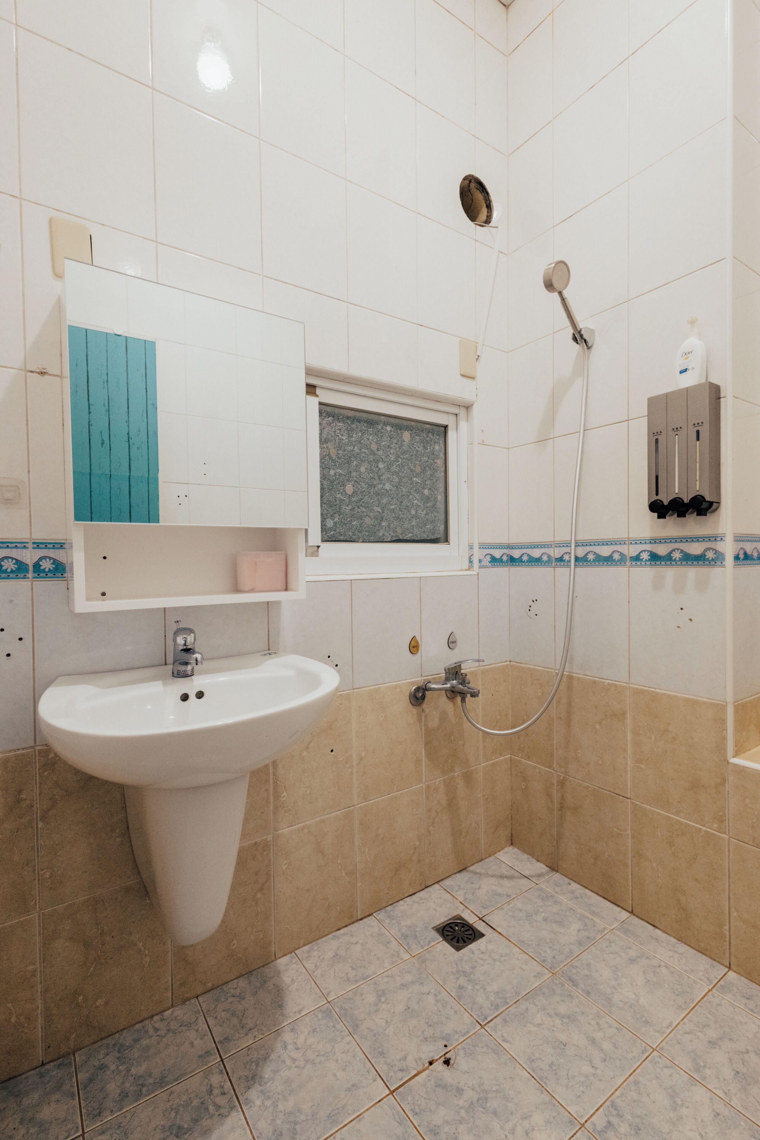 Un baño con lavamanos, ventana, ducha y dispensador de jabón.