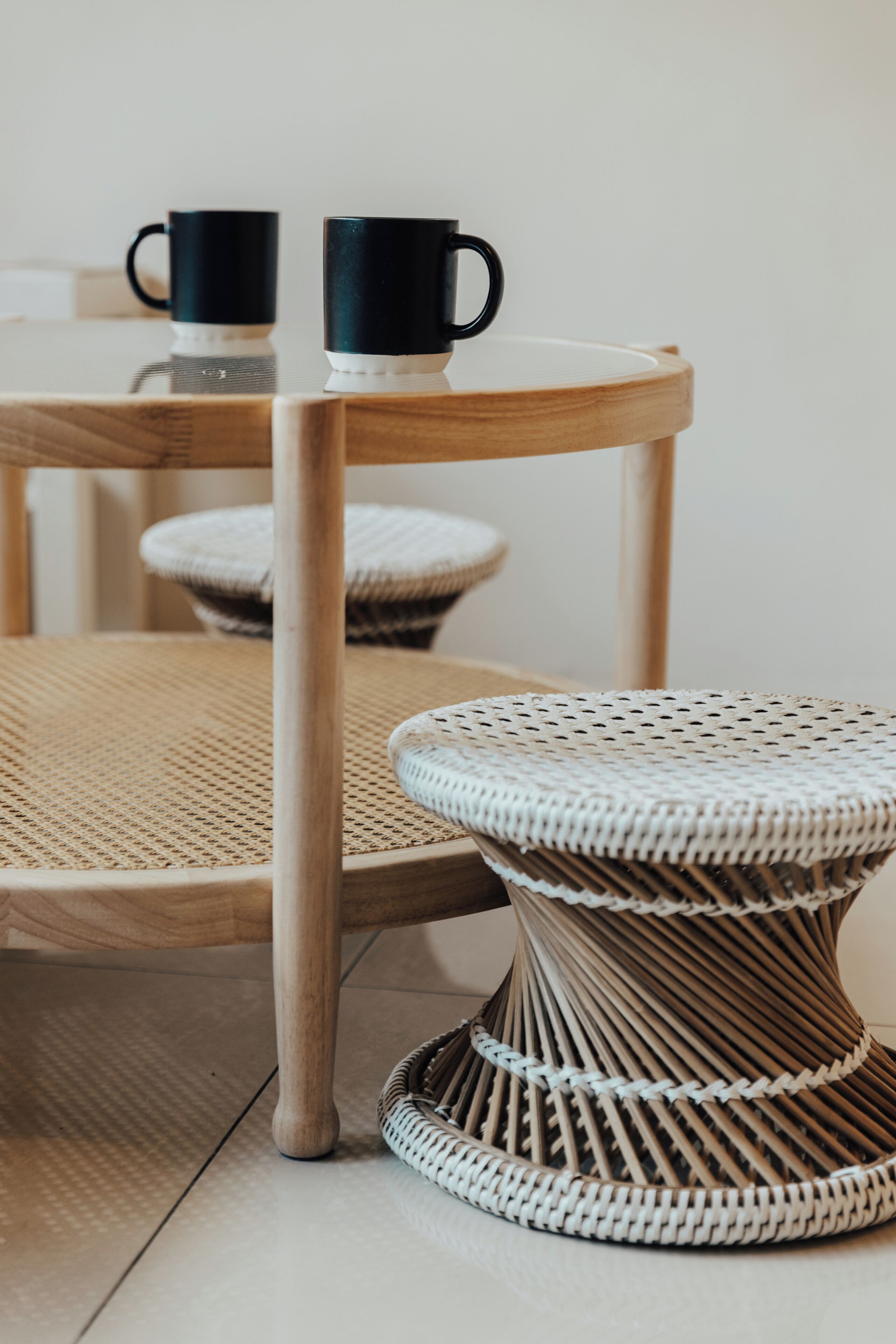 A wicker chair and stool with a table and two black mugs on it.