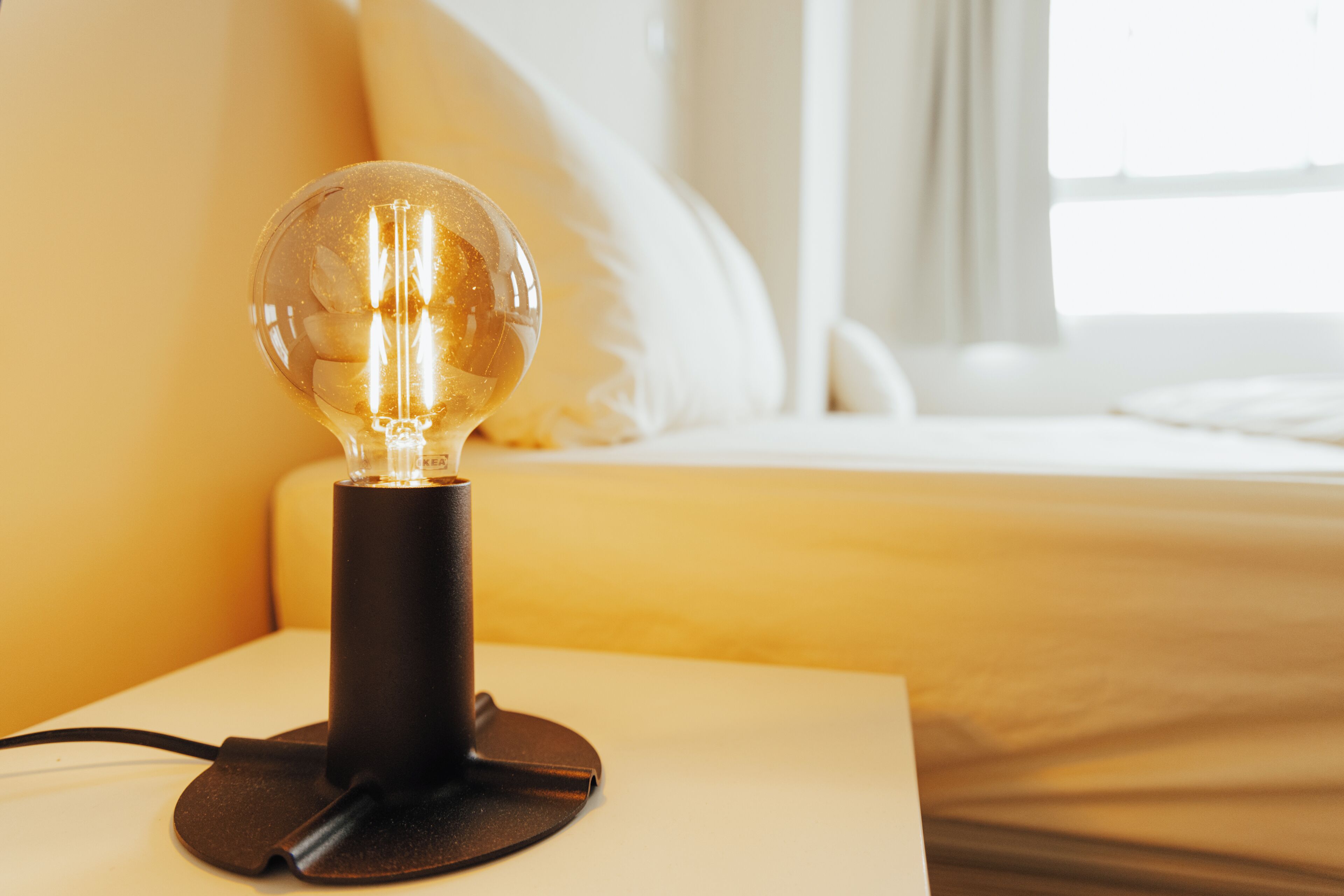 Una mesita de noche con una lámpara de vidrio transparente, base negra y cable de alimentación.