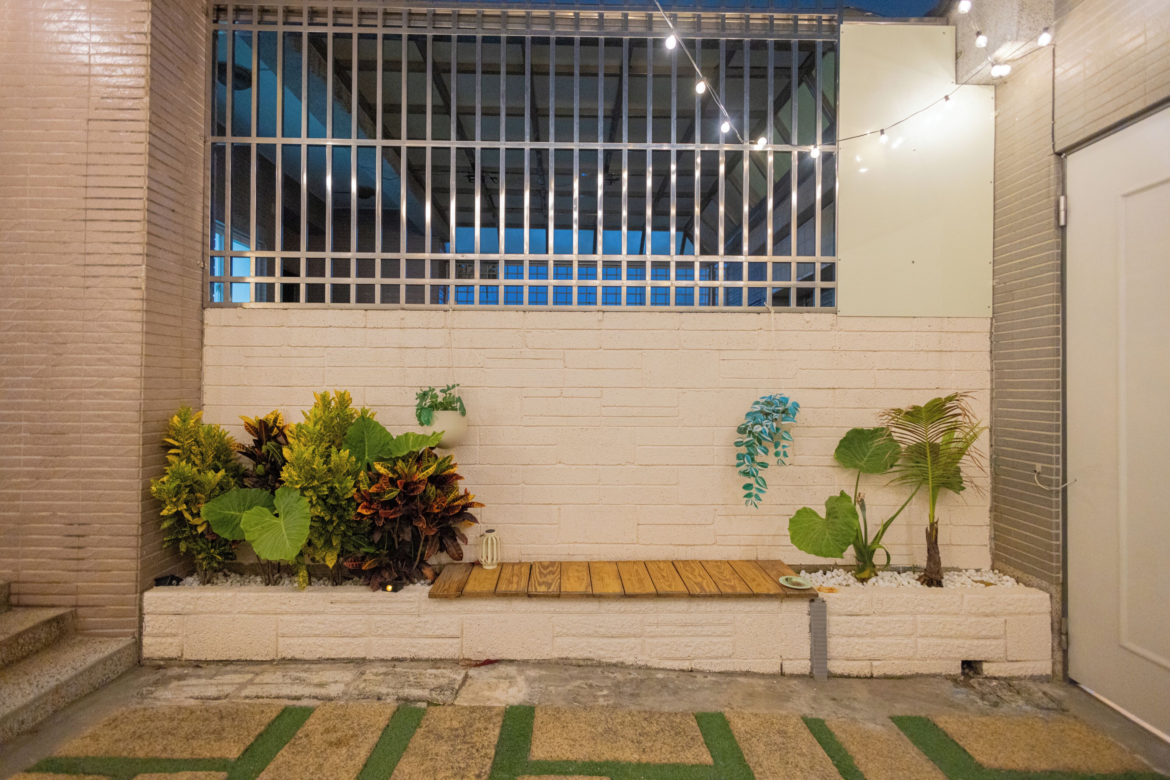 Un pequeño espacio al aire libre con un muro de ladrillo blanco, un banco de madera y varias plantas en macetas.