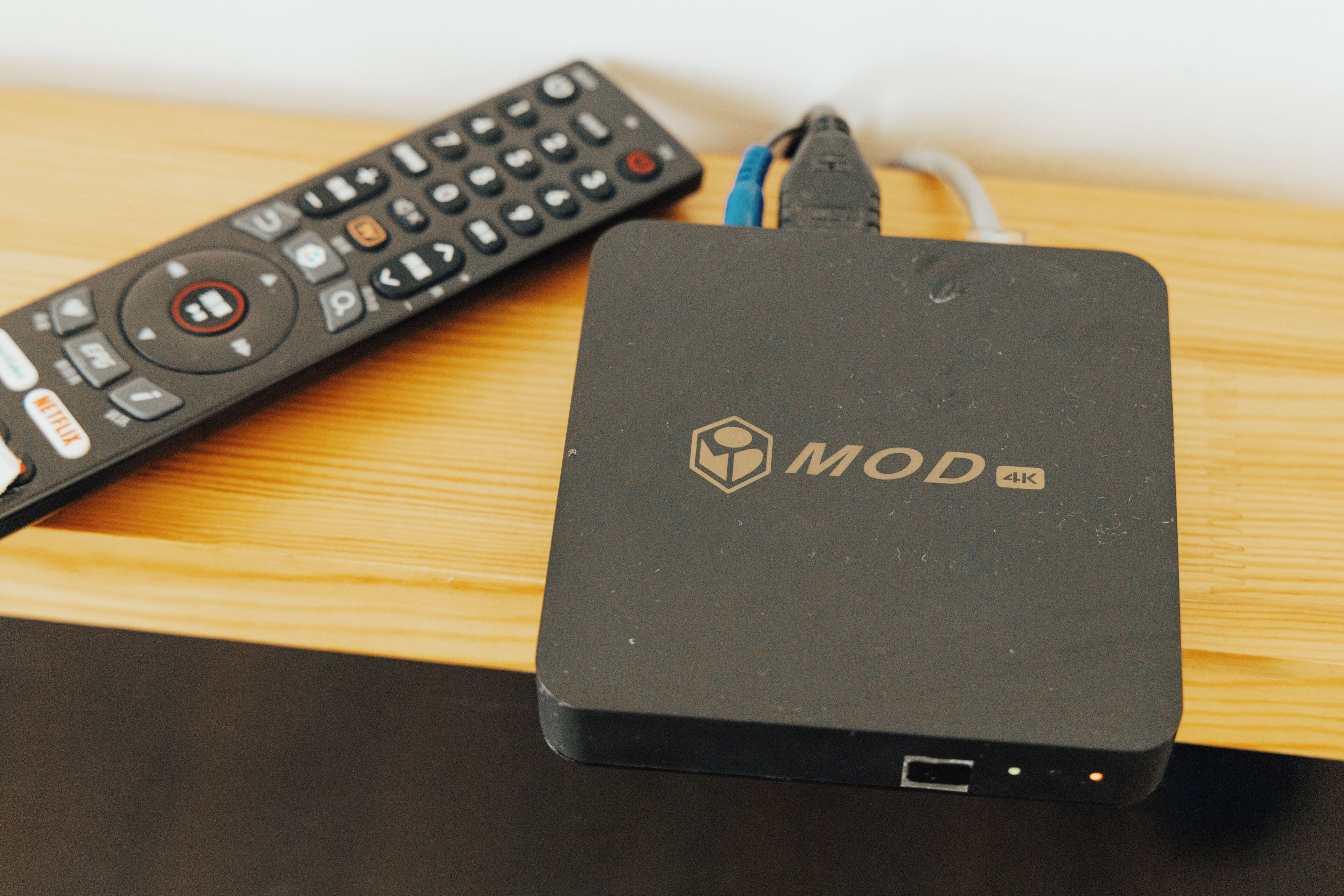 A black MOD 4K device with a remote control beside it on a wooden surface.