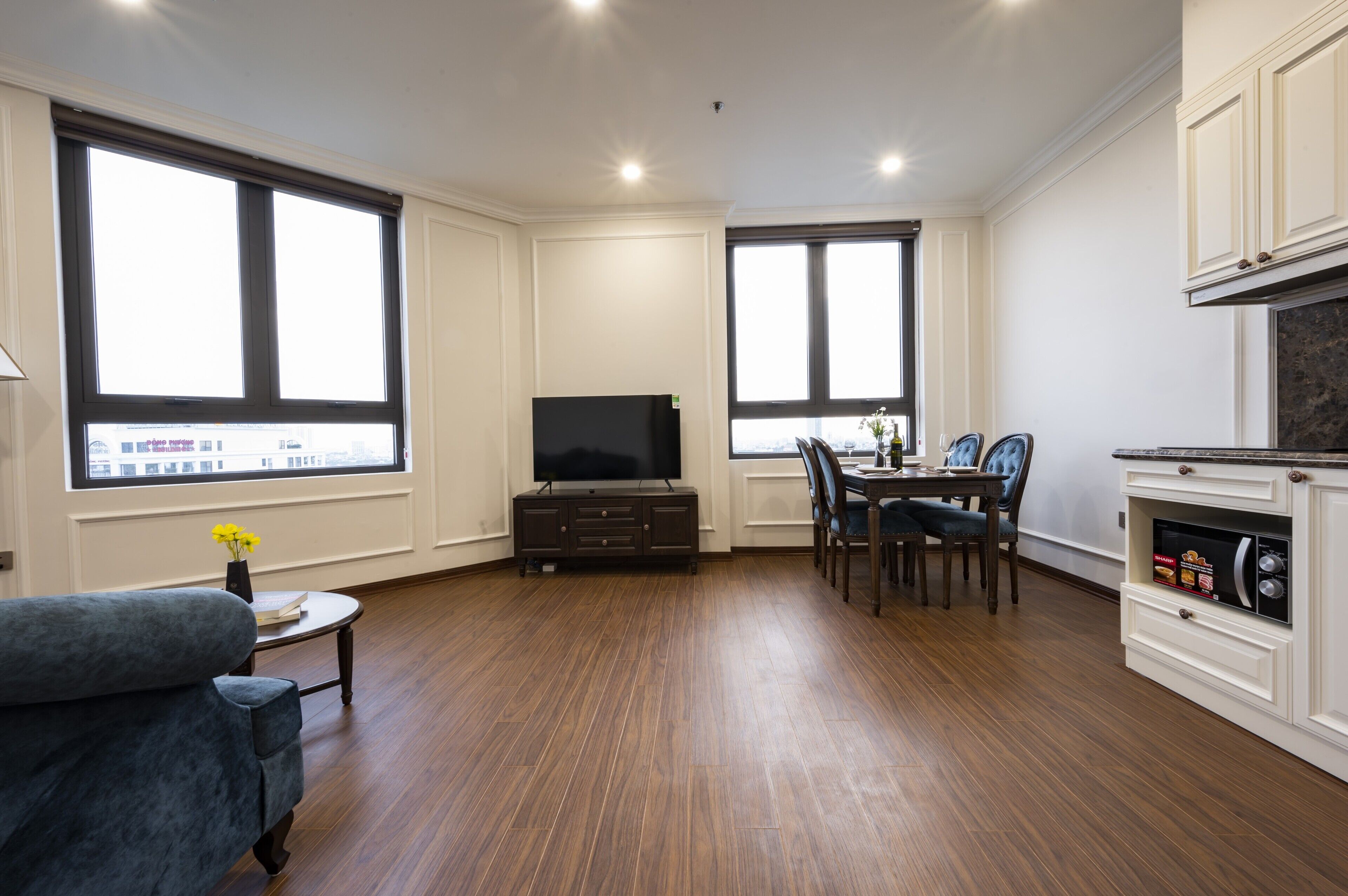 A living room with a flat-screen TV, a dining table with chairs, and a kitchen area with a microwave.