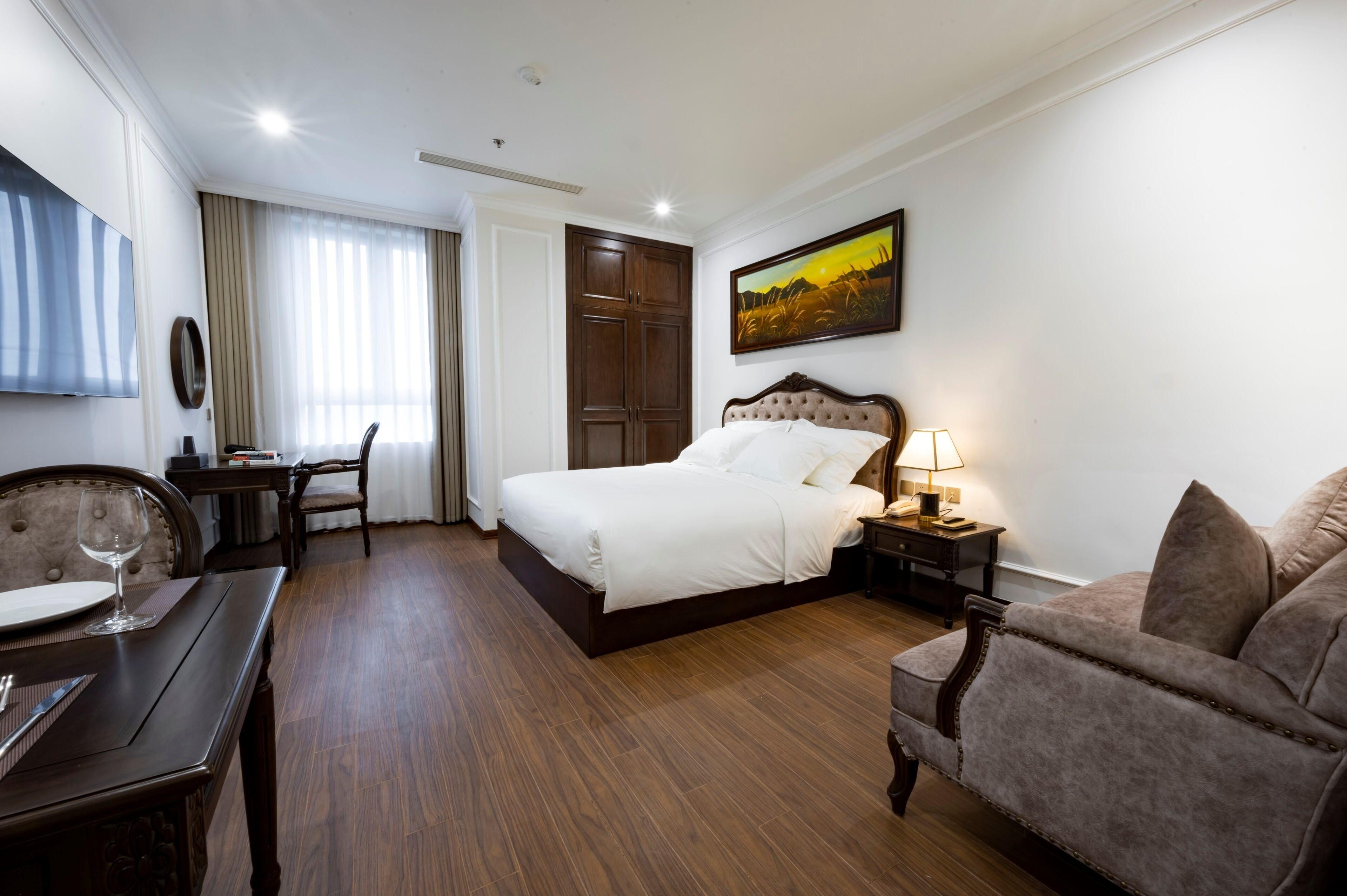 A hotel room with a bed, a desk with a chair, a sofa, and a TV on the wall.