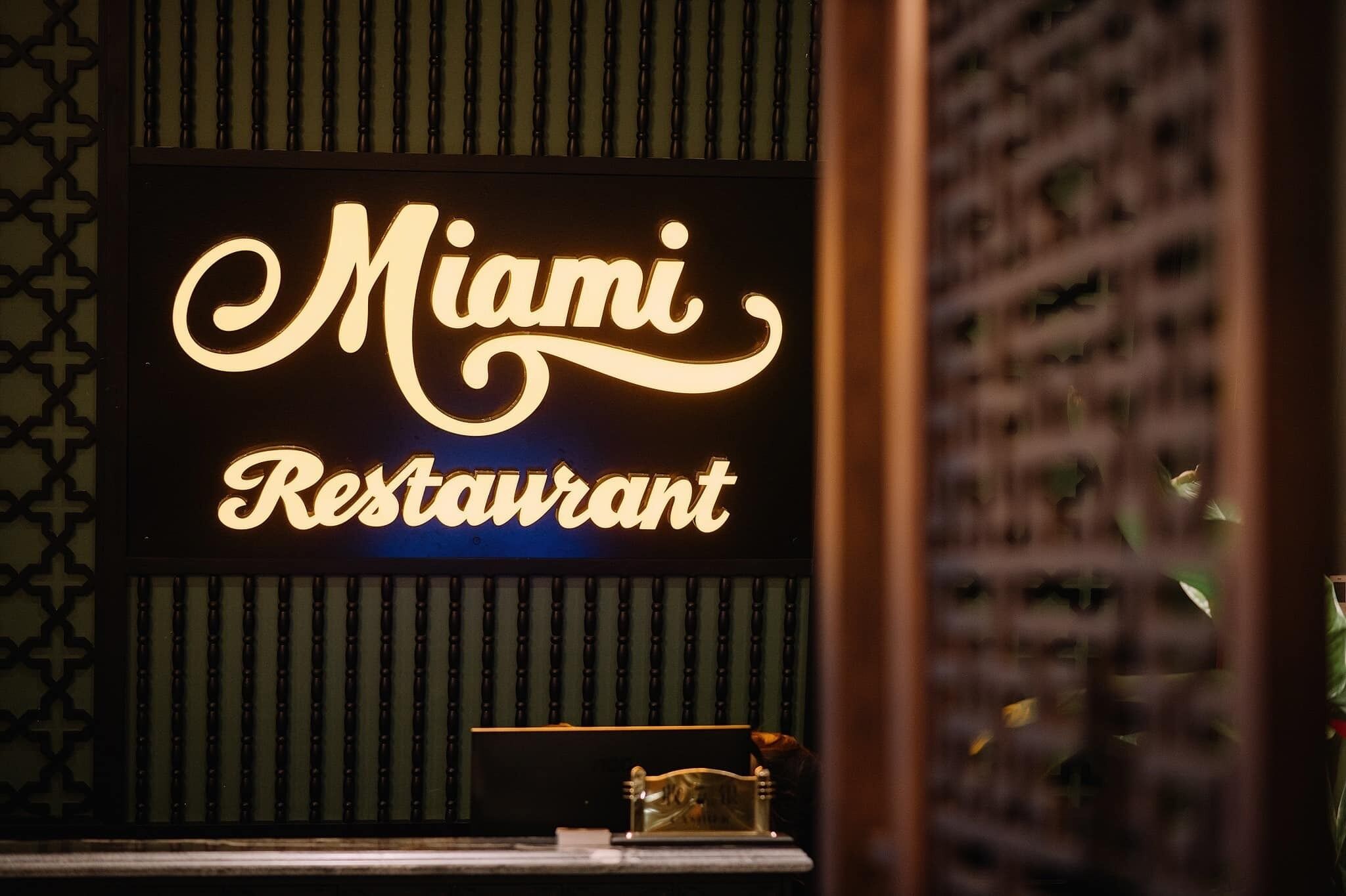 A neon sign for 'Miami Restaurant' with a patterned wall and a small table with a decorative item.