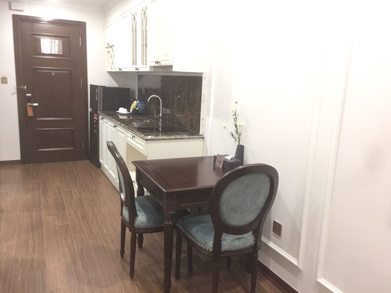 A compact kitchen with a dark countertop, white cabinets, and a dining area with a wooden table and chairs.