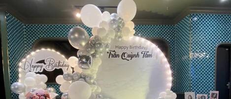 A birthday celebration setup with balloons, a large illuminated sign, and gift boxes.