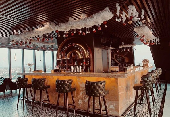 Eine Bar mit Marmorzauber, Lederbarkreuzchen und Blick auf die Stadt durch große Fenster.