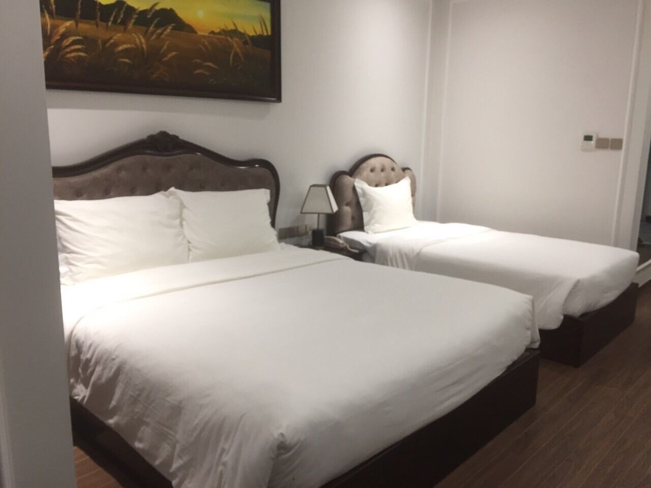 Una habitación de hotel con dos camas individuales, una mesita de noche con lámpara y un cuadro en la pared.