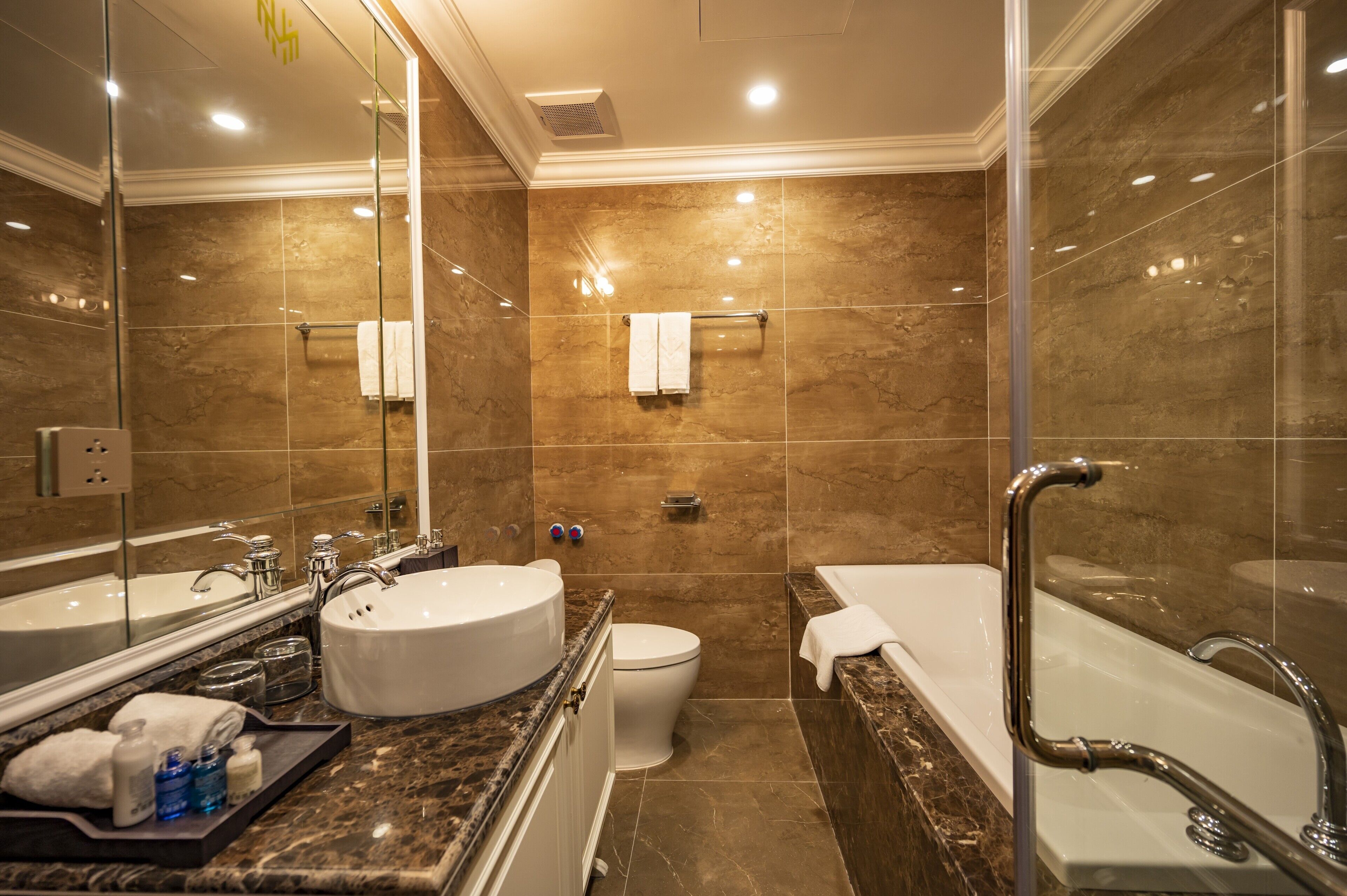A modern bathroom with a large mirror, a bathtub, a toilet, and a vanity with a sink and mirror.