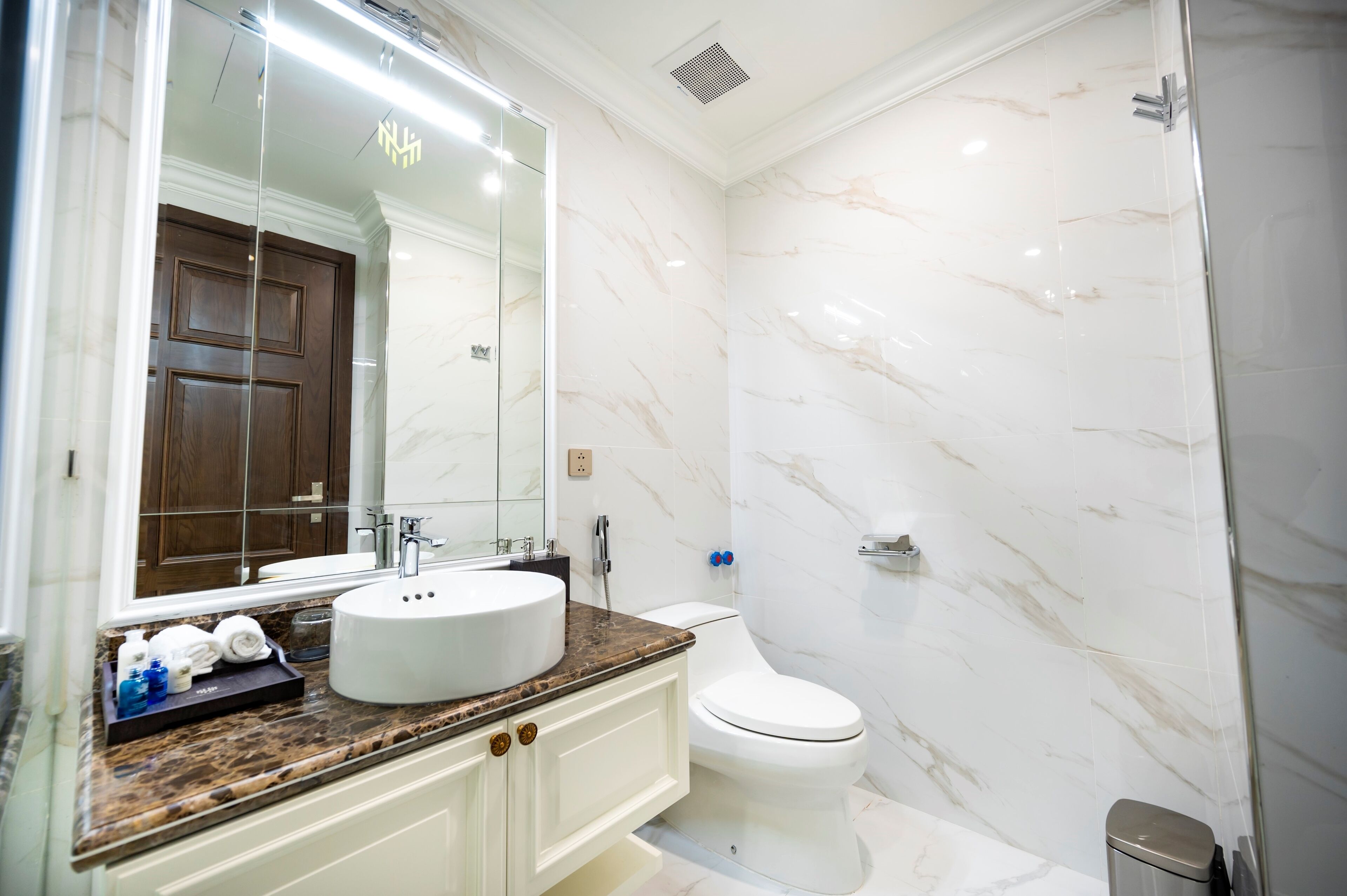 A bathroom with a marble wall, a sink, a toilet, and a mirror.